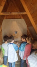 Foto: Kinder in einer improvisierten "Steinzeithöhle" betrachten ein Stück Tapete voller bunter, steinzeit-artiger kindlicher Motive und Handabdrücke auf einer Holzwand