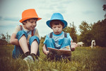 Foto: zwei kleine Kinder sitzen auf einer Wiese und lesen gemeinsam ein Buch