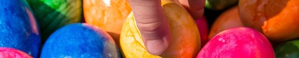 Foto: Eine Hand greift ein Osterei aus einer Menge bunter Ostereier