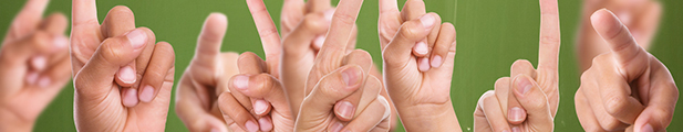 Eine Anzahl von Kinderhänden beim Melden ("Aufzeigen"); nur die Hände (ohne Arme), vor grünem Hintergrund (Schultafel).